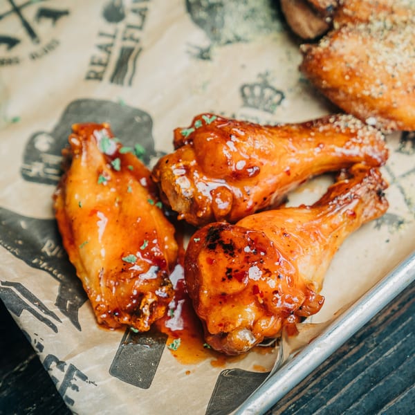 Three Salty Joe's BBQ chicken wings, glazed with sauce and garnished with herbs, on branded parchment paper.