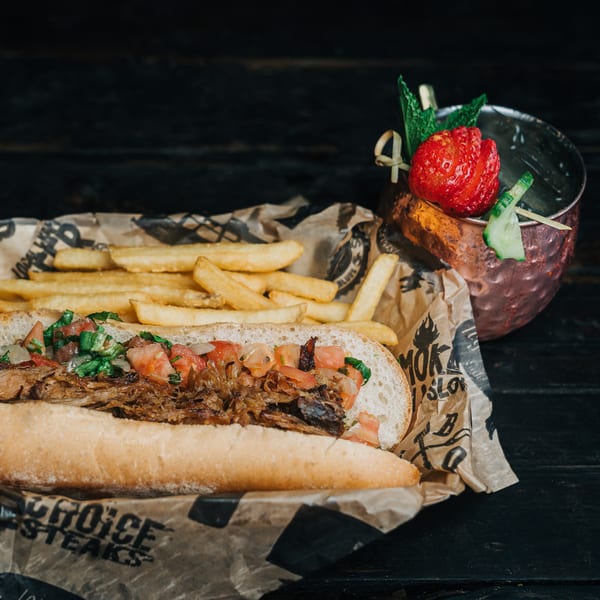 Salty Joe's BBQ pulled pork sandwich with fries and a garnished cocktail on a dark wooden table.