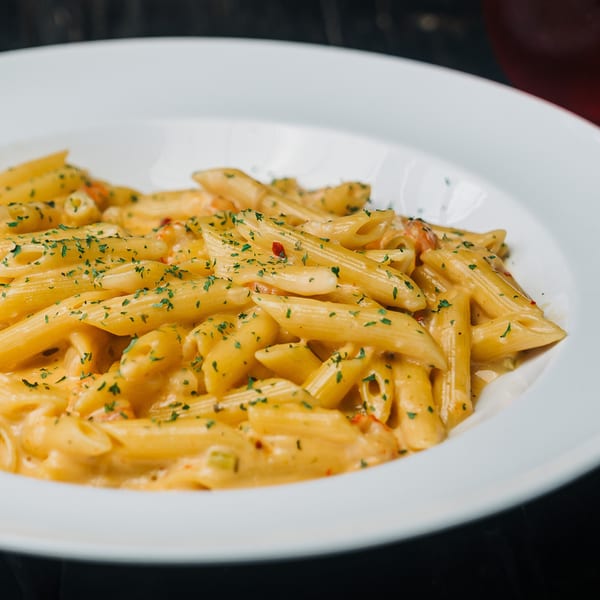 Creamy penne pasta with herbs and red pepper flakes in a white bowl.