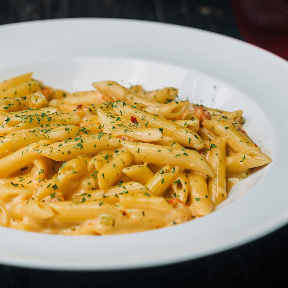Creamy penne pasta with herbs and red pepper flakes in a white bowl.