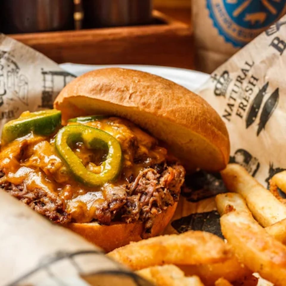 Salty Joe's BBQ pulled pork sandwich with melted cheese and jalapeños, served with fries.
